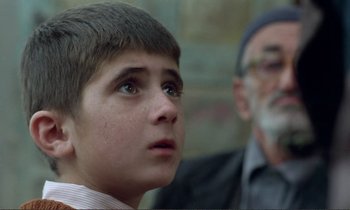 Movie still from “Where Is the Friend's House?” (1987), directed by Abbas Kiarostami – A young boy looking up at the sky with an older man in the background; Close Up shot, Low angle