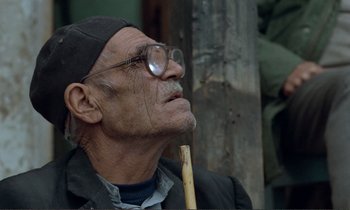 Movie still from “Where Is the Friend's House?” (1987), directed by Abbas Kiarostami – An old man wearing glasses and holding a wooden stick; Close Up shot, Low angle