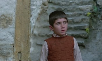 Movie still from “Where Is the Friend's House?” (1987), directed by Abbas Kiarostami – A young boy wearing a red vest looking to his left; Close Up shot, Over the shoulder angle