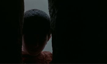 Movie still from “Where Is the Friend's House?” (1987), directed by Abbas Kiarostami – A young boy is hiding behind a wall; Close Up shot, Low angle