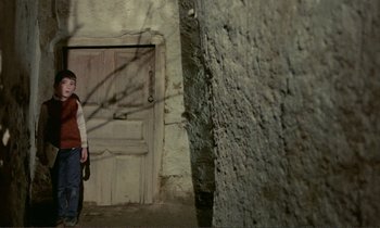 Movie still from “Where Is the Friend's House?” (1987), directed by Abbas Kiarostami – A person standing in front of a door; Wide shot, High angle