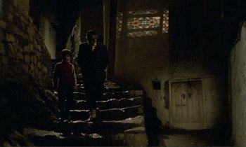 Movie still from “Where Is the Friend's House?” (1987), directed by Abbas Kiarostami – A man and a boy walking up some stairs; Wide shot, Low angle