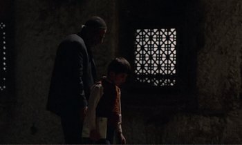 Movie still from “Where Is the Friend's House?” (1987), directed by Abbas Kiarostami – A man and a boy are walking in the dark; Wide shot, Low angle
