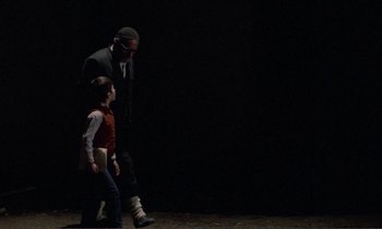 Movie still from “Where Is the Friend's House?” (1987), directed by Abbas Kiarostami – A man and a boy are walking in a dark room; Wide shot, Over the shoulder angle