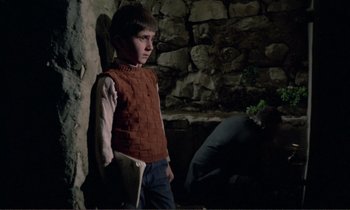 Movie still from “Where Is the Friend's House?” (1987), directed by Abbas Kiarostami – A young boy standing next to a stone wall; Medium shot, High angle