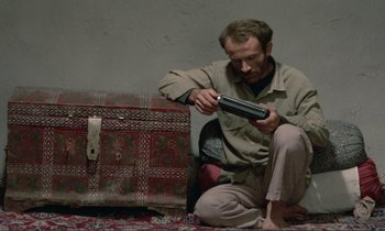Movie still from “Where Is the Friend's House?” (1987), directed by Abbas Kiarostami – A man sitting on the ground holding a video game controller; Medium shot, High angle