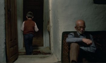 Movie still from “Where Is the Friend's House?” (1987), directed by Abbas Kiarostami – An older man and a young boy in a doorway; Wide shot, High angle