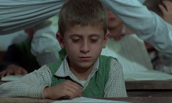 Movie still from “Where Is the Friend's House?” (1987), directed by Abbas Kiarostami – A young boy writing on a piece of paper; Medium shot, Over the shoulder angle