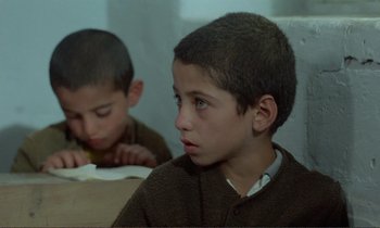Movie still from “Where Is the Friend's House?” (1987), directed by Abbas Kiarostami – Two young boys sitting at a table with a book in front of them; Close Up shot, High angle