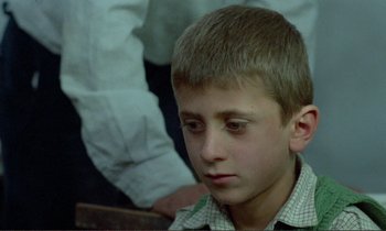 Movie still from “Where Is the Friend's House?” (1987), directed by Abbas Kiarostami – A young boy sitting in front of a group of people; Close Up shot, High angle