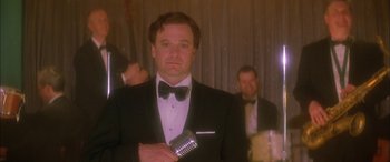 Movie still from “Where the Truth Lies” (2005), directed by Atom Egoyan – A man in a tuxedo holding a microphone in his hand; Close Up shot, Low angle