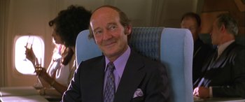 Movie still from “Where the Truth Lies” (2005), directed by Atom Egoyan – A man in a suit and tie sitting in an airplane seat; Close Up shot, Over the shoulder angle