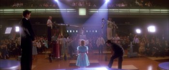 Movie still from “Where the Truth Lies” (2005), directed by Atom Egoyan – A girl in a blue dress standing in front of an audience; Wide shot, Low angle
