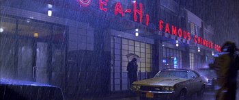 Movie still from “Where the Truth Lies” (2005), directed by Atom Egoyan – A person holding an umbrella while standing in front of a building; Wide shot, Low angle