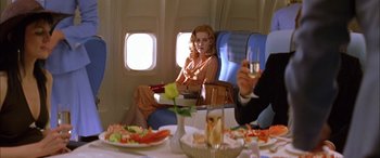 Movie still from “Where the Truth Lies” (2005), directed by Atom Egoyan – A woman sitting at a table on an airplane with a glass of wine; Medium shot, Over the shoulder angle