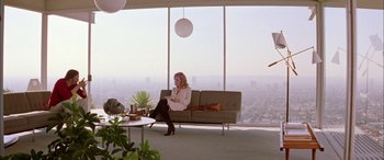 Movie still from “Where the Truth Lies” (2005), directed by Atom Egoyan – A woman sitting on top of a couch in front of a window; Wide shot, Low angle