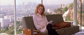 Movie still from “Where the Truth Lies” (2005), directed by Atom Egoyan – A woman sitting on top of a couch reading a magazine; Medium shot, High angle