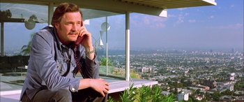 Movie still from “Where the Truth Lies” (2005), directed by Atom Egoyan – A man sitting in front of a window on a cell phone; Medium shot, Low angle