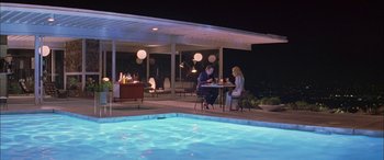 Movie still from “Where the Truth Lies” (2005), directed by Atom Egoyan – A man and a woman sitting at a table by a pool; Extreme Wide shot, High angle
