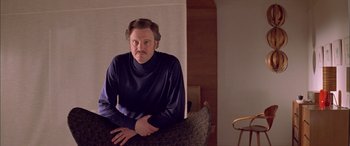 Movie still from “Where the Truth Lies” (2005), directed by Atom Egoyan – A man with a beard is leaning on a couch; Medium shot, Low angle