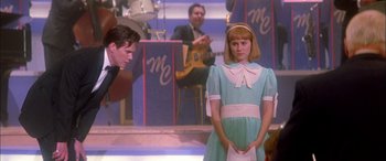 Movie still from “Where the Truth Lies” (2005), directed by Atom Egoyan – A girl in a blue dress standing in front of a band; Medium shot, Over the shoulder angle