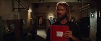 Movie still from “Whip It” (2009), directed by Drew Barrymore – A man with long hair and a beard holding a red book; Close Up shot, Low angle