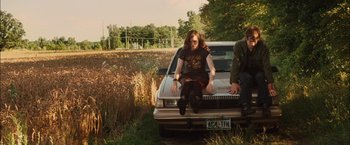 Movie still from “Whip It” (2009), directed by Drew Barrymore – A woman sitting on the back of a car next to a man; Wide shot, Low angle