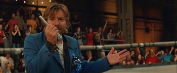 Movie still from “Whip It” (2009), directed by Drew Barrymore – A man in a blue jacket holding a microphone in front of a group of people; Close Up shot, Over the shoulder angle