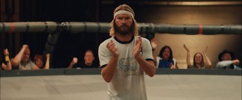Movie still from “Whip It” (2009), directed by Drew Barrymore – A man with long blond hair and a headband clapping; Medium shot, Low angle