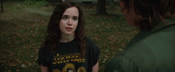 Movie still from “Whip It” (2009), directed by Drew Barrymore – A woman with long brown hair wearing a t - shirt with the name stryper on it; Close Up shot, Over the shoulder angle