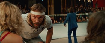 Movie still from “Whip It” (2009), directed by Drew Barrymore – A man with long hair and a headband is crouched down; Close Up shot, Low angle
