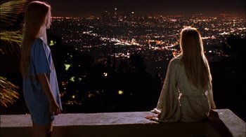Movie still from “White Oleander” (2002), directed by Peter Kosminsky – A woman sitting on a ledge looking at a city at night; Wide shot, High angle