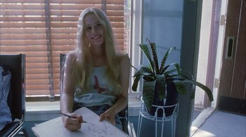 Movie still from “White Oleander” (2002), directed by Peter Kosminsky – A woman sitting at a table with a plant in front of a window; Medium shot, Over the shoulder angle