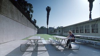 Movie still from “White Oleander” (2002), directed by Peter Kosminsky – A person sitting on a bench near some picnic tables; Extreme Wide shot, High angle