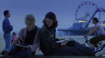 Movie still from “White Oleander” (2002), directed by Peter Kosminsky – Two people sitting on the beach looking at a tablet; Medium shot, Low angle