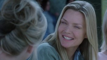 Movie still from “White Oleander” (2002), directed by Peter Kosminsky – A woman smiling at another woman in front of a group of people; Close Up shot, Over the shoulder angle