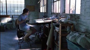 Movie still from “White Oleander” (2002), directed by Peter Kosminsky – A woman sitting at a table in a room; Wide shot, High angle