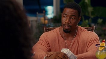Movie still from “Why Did I Get Married Too?” (2010), directed by Tyler Perry – A man sitting at a table holding a stack of money; Medium shot, Over the shoulder angle