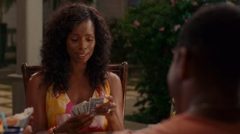 Movie still from “Why Did I Get Married Too?” (2010), directed by Tyler Perry – A woman sitting at a table holding a stack of money; Medium shot, Over the shoulder angle