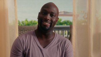 Movie still from “Why Did I Get Married Too?” (2010), directed by Tyler Perry – A man smiling for the camera while wearing a purple t - shirt; Close Up shot, High angle