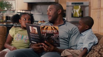 Movie still from “Why Did I Get Married Too?” (2010), directed by Tyler Perry – A man sitting on a couch reading a book to two children; Medium shot, Over the shoulder angle
