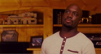 Movie still from “Why Did I Get Married?” (2007), directed by Tyler Perry – A man standing in front of a shelf in a living room; Close Up shot, Over the shoulder angle