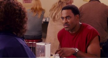 Movie still from “Why Did I Get Married?” (2007), directed by Tyler Perry – A man sitting at a table in front of other people; Close Up shot, Over the shoulder angle