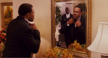 Movie still from “Why Did I Get Married?” (2007), directed by Tyler Perry – A man adjusting his tie in front of a mirror; Medium shot, Over the shoulder angle