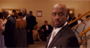 Movie still from “Why Did I Get Married?” (2007), directed by Tyler Perry – A man in a suit and tie in front of other people; Close Up shot, Over the shoulder angle