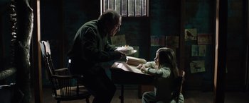 Movie still from “Wildling” (2018), directed by Fritz Böhm – An older man and a young girl sitting at a table; Medium shot, Over the shoulder angle