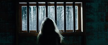 Movie still from “Wildling” (2018), directed by Fritz Böhm – A woman standing in front of a window with snow outside; Medium shot, Low angle