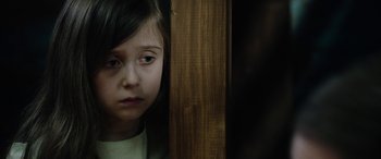 Movie still from “Wildling” (2018), directed by Fritz Böhm – A little girl sitting in front of a wooden wall; Close Up shot, Over the shoulder angle