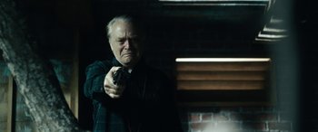 Movie still from “Wildling” (2018), directed by Fritz Böhm – An older man holding a gun in a dark room; Close Up shot, Over the shoulder angle