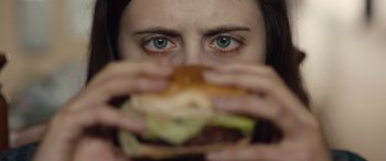 Movie still from “Wildling” (2018), directed by Fritz Böhm – A woman is holding up a hamburger to her face; Extreme Close Up shot, Overhead angle